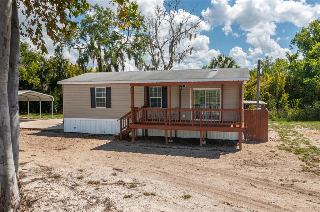 A single-story mobile home with a wooden front deck and a metal carport — 991 BAY COURT, FROSTPROOF, FL