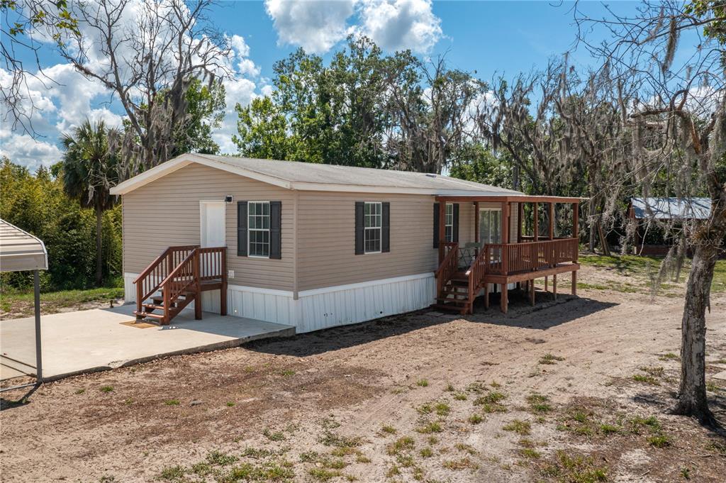 A tan mobile home with a wooden deck and a concrete patio sits on dirt — 991 BAY COURT, FROSTPROOF, FL