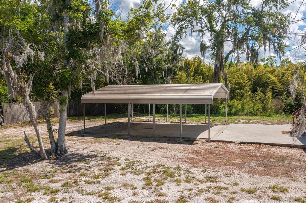 A metal carport stands on a concrete pad in a wooded backyard — 991 BAY COURT, FROSTPROOF, FL