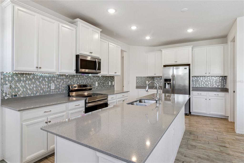 A modern kitchen features white cabinets, gray quartz countertops, stainless steel appliances, and a backsplash — 4168 SOLAMOR STREET, LAKELAND, FL