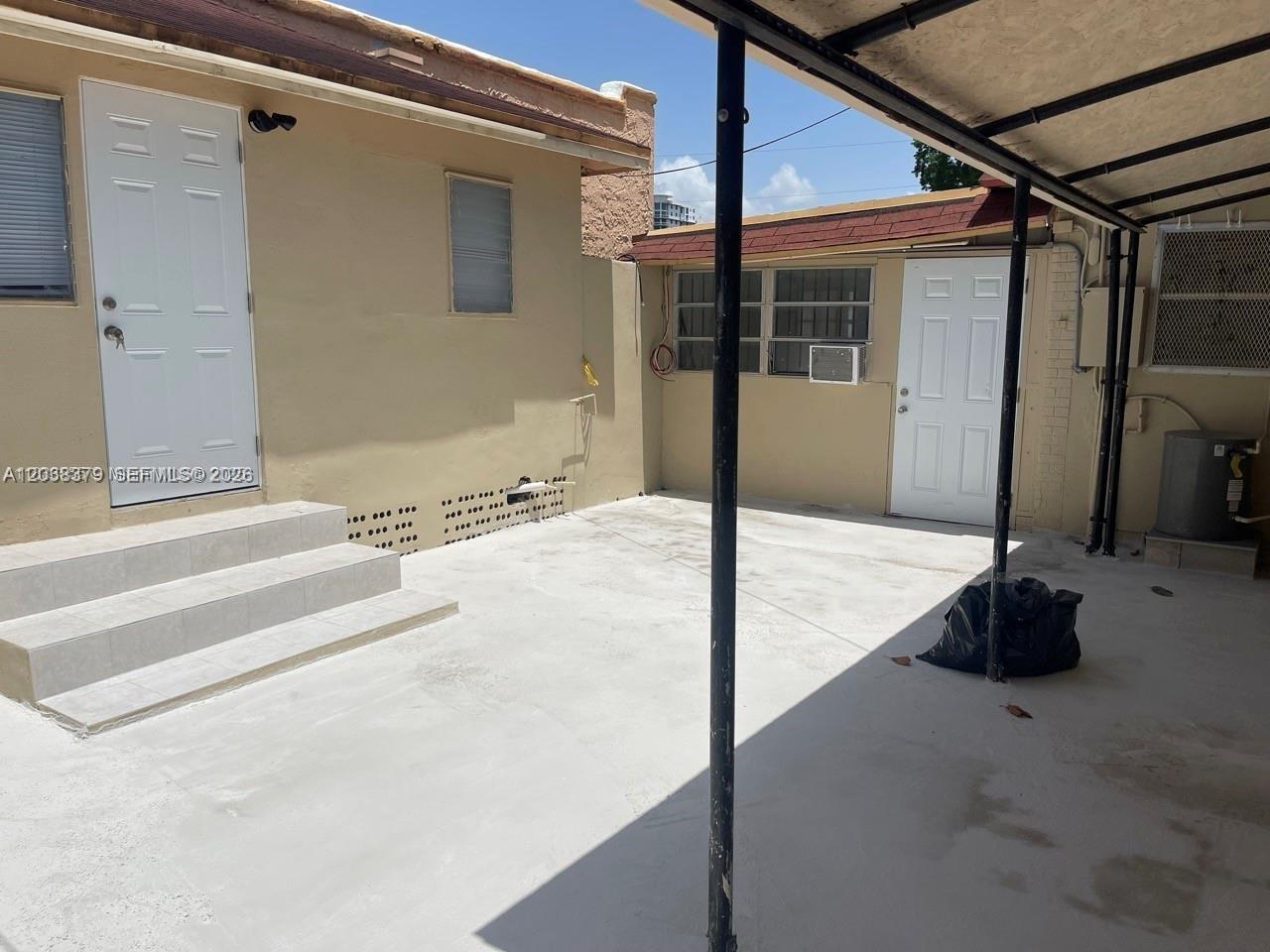 A paved outdoor patio area sits between two beige buildings with white doors and a carport — 219 SW 21st Ave # 3, Miami FL 33135, MIAMI, FL