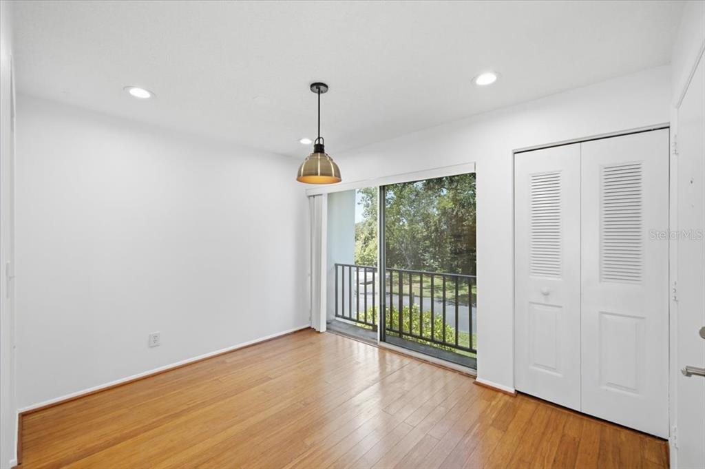 A room with hardwood floors, a hanging pendant light, and a sliding glass door to a balcony — 2060 MARILYN STREET UNIT 236, CLEARWATER, FL