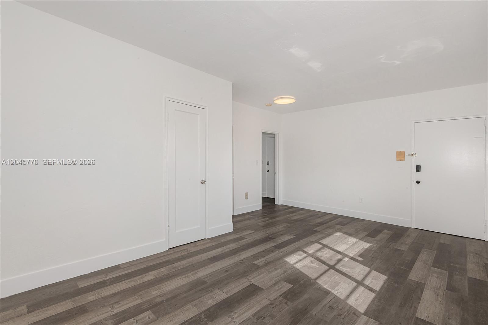 An empty room features white walls, dark wood-look flooring, and two white interior doors — 8340 Crespi Blvd # 20, Miami Beach FL 33141, MIAMI BEACH, FL