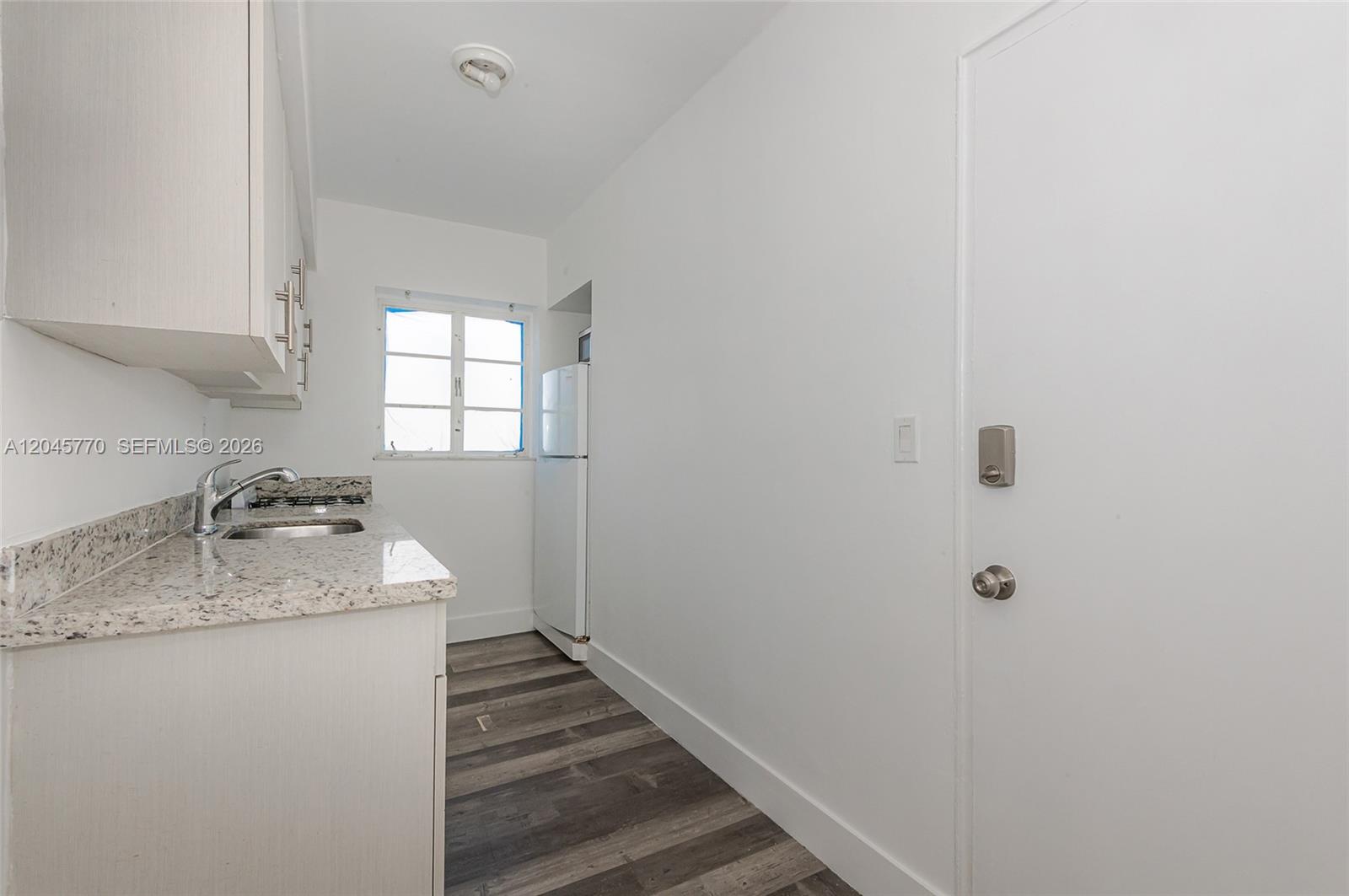 A narrow kitchen features white cabinets, granite countertops, a refrigerator, and wood-look flooring — 8340 Crespi Blvd # 20, Miami Beach FL 33141, MIAMI BEACH, FL