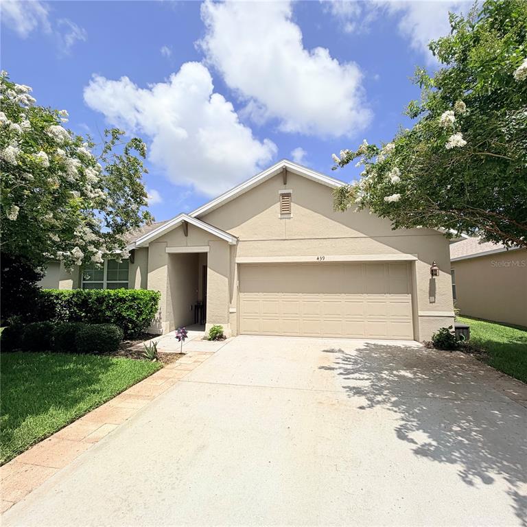 A single-story house with a beige stucco exterior, a two-car garage, and blooming trees — 439 PINK CORAL LANE, NEW SMYRNA BEACH, FL