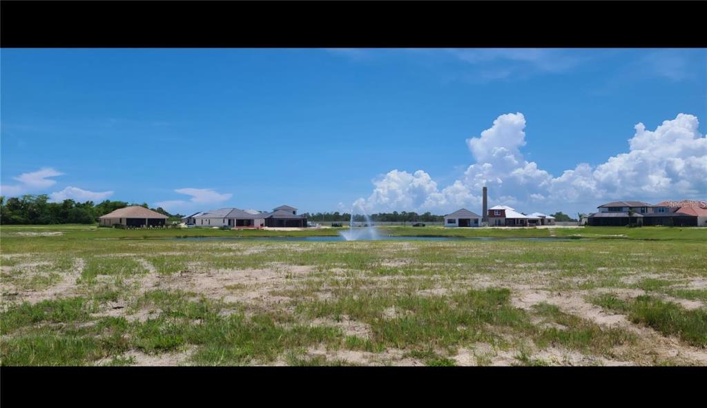 A vacant lot overlooks a small pond with a fountain and several houses in the distance — 21 DEL PALMA DRIVE, PALM COAST, FL