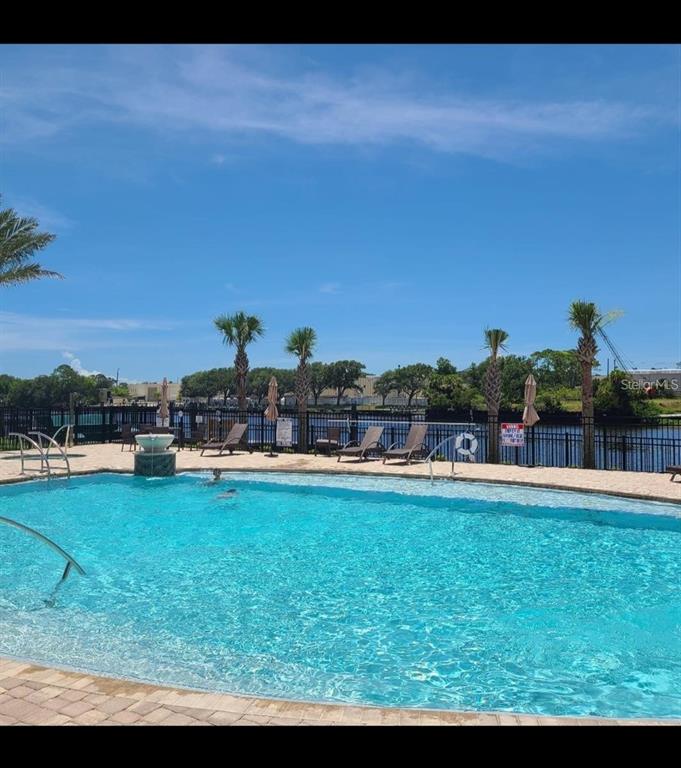 A swimming pool with lounge chairs and palm trees overlooks a canal and fence — 21 DEL PALMA DRIVE, PALM COAST, FL