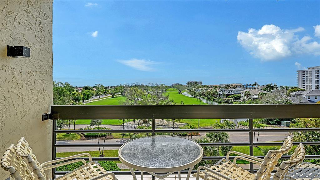 A balcony with a glass table and chairs overlooks a golf course and distant buildings — 1085 GULF OF MEXICO DRIVE UNIT 404, LONGBOAT KEY, FL