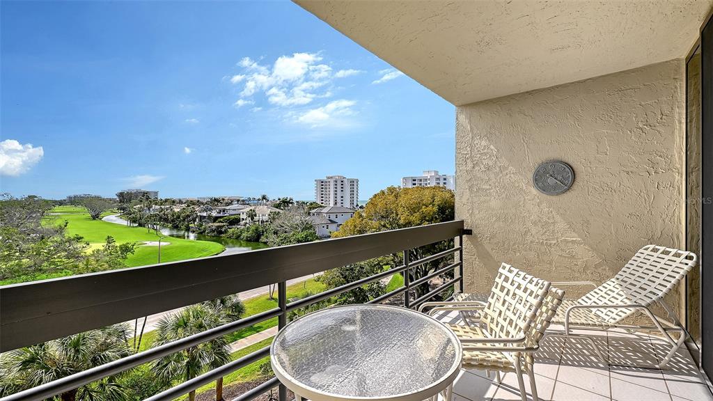 A balcony with patio furniture overlooks a golf course, water, and distant buildings — 1085 GULF OF MEXICO DRIVE UNIT 404, LONGBOAT KEY, FL