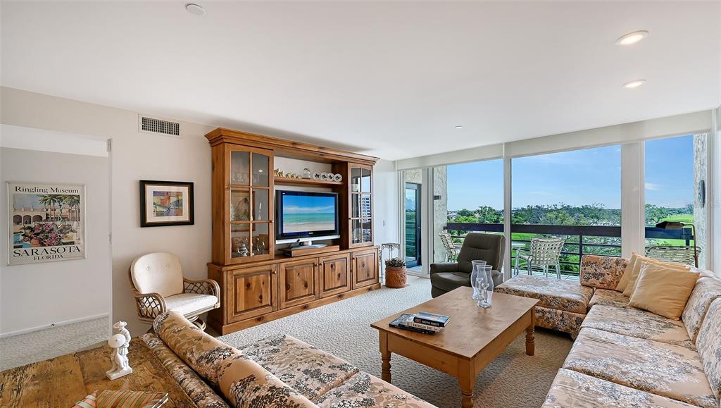 A living room features a large wooden entertainment center, patterned sectional sofa, and floor-to-ceiling windows — 1085 GULF OF MEXICO DRIVE UNIT 404, LONGBOAT KEY, FL
