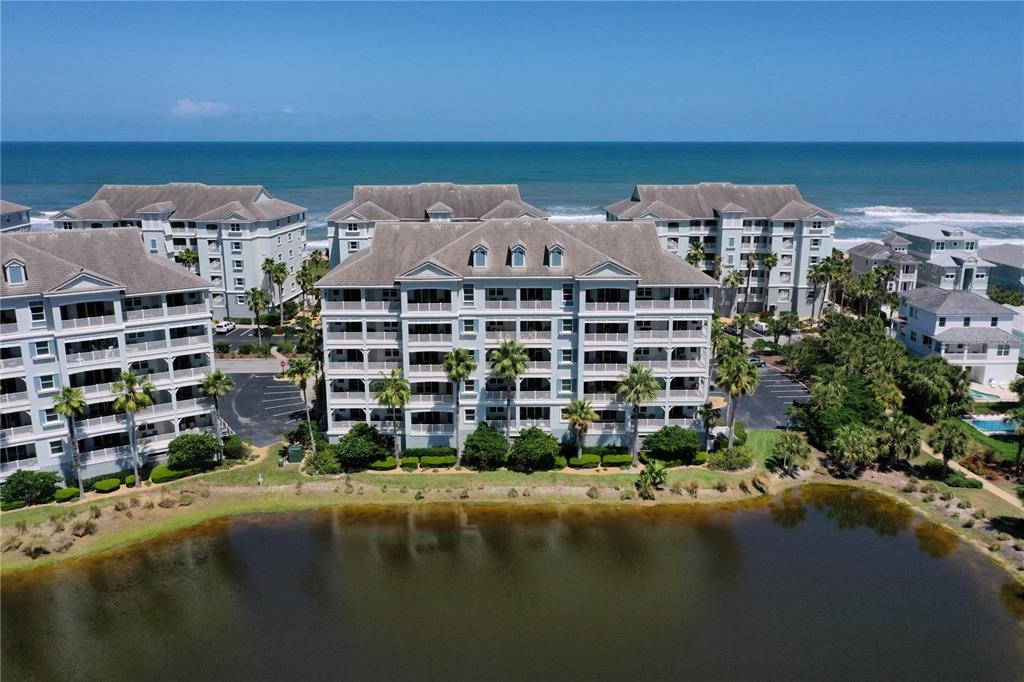 An aerial view shows multi-story apartment buildings situated between a pond and the ocean — 1000 CINNAMON BEACH WAY UNIT 942, PALM COAST, FL