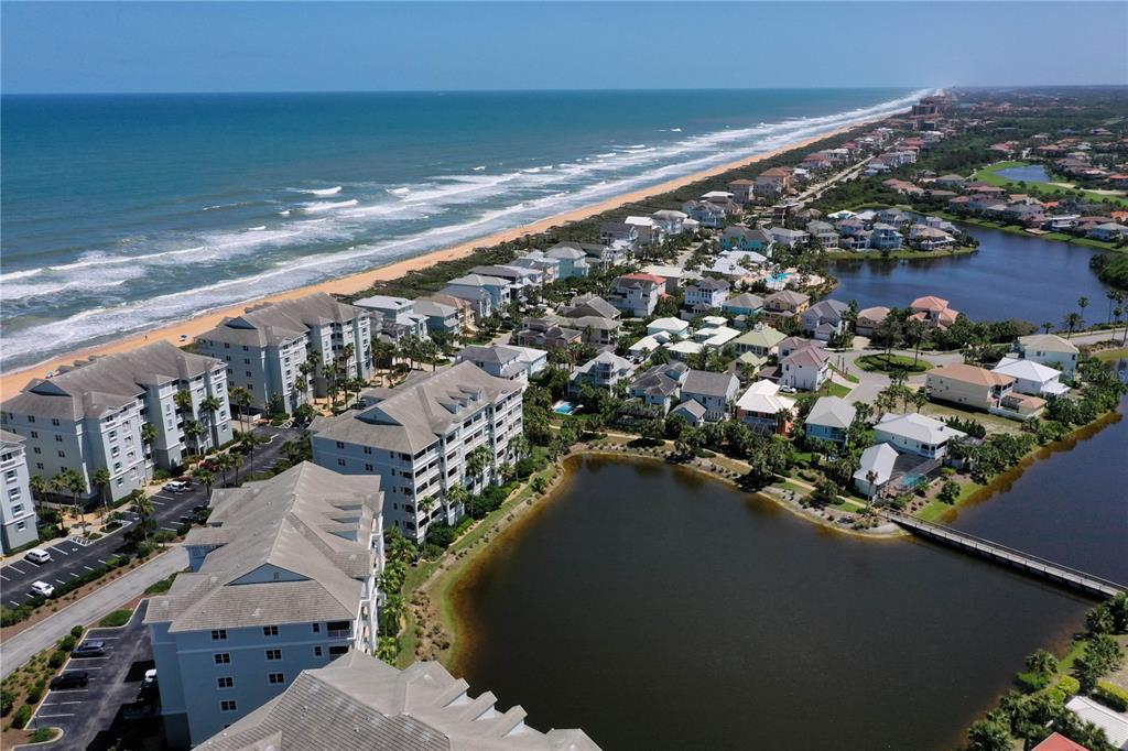 An aerial view shows a coastal neighborhood with multi-story buildings, houses, and a large pond — 1000 CINNAMON BEACH WAY UNIT 942, PALM COAST, FL
