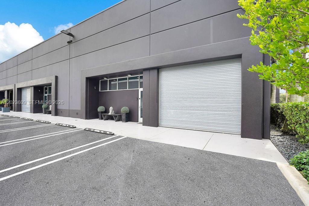 The exterior of a commercial building features a gray facade, a roll-up door, and parking — 6030 NW 102nd Ave # 211, Doral FL 33178, DORAL, FL