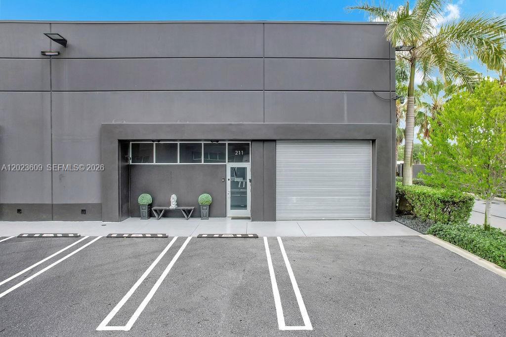 A gray commercial building exterior features a glass door, a roll-up gate, and parking spaces — 6030 NW 102nd Ave # 211, Doral FL 33178, DORAL, FL