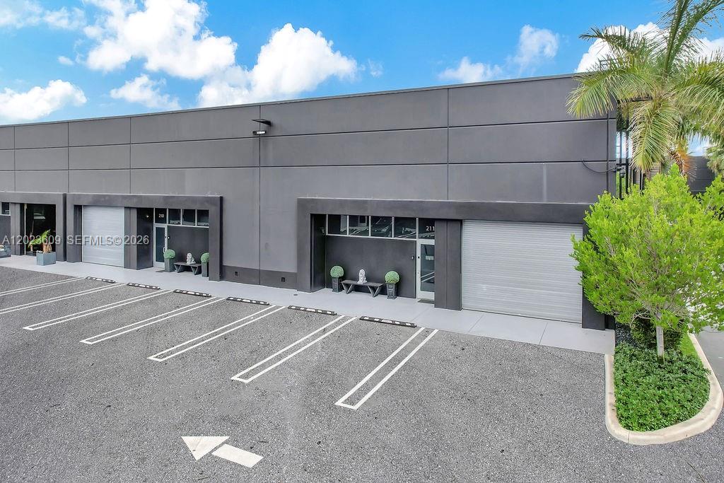 The exterior of a modern gray commercial building features multiple roll-up doors and parking spaces — 6030 NW 102nd Ave # 211, Doral FL 33178, DORAL, FL