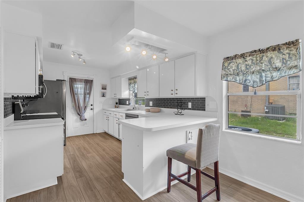 A kitchen with white cabinets, a dark tile backsplash, wood-look flooring, and a breakfast bar — 320 S SEMINOLE AVENUE, LAKE ALFRED, FL