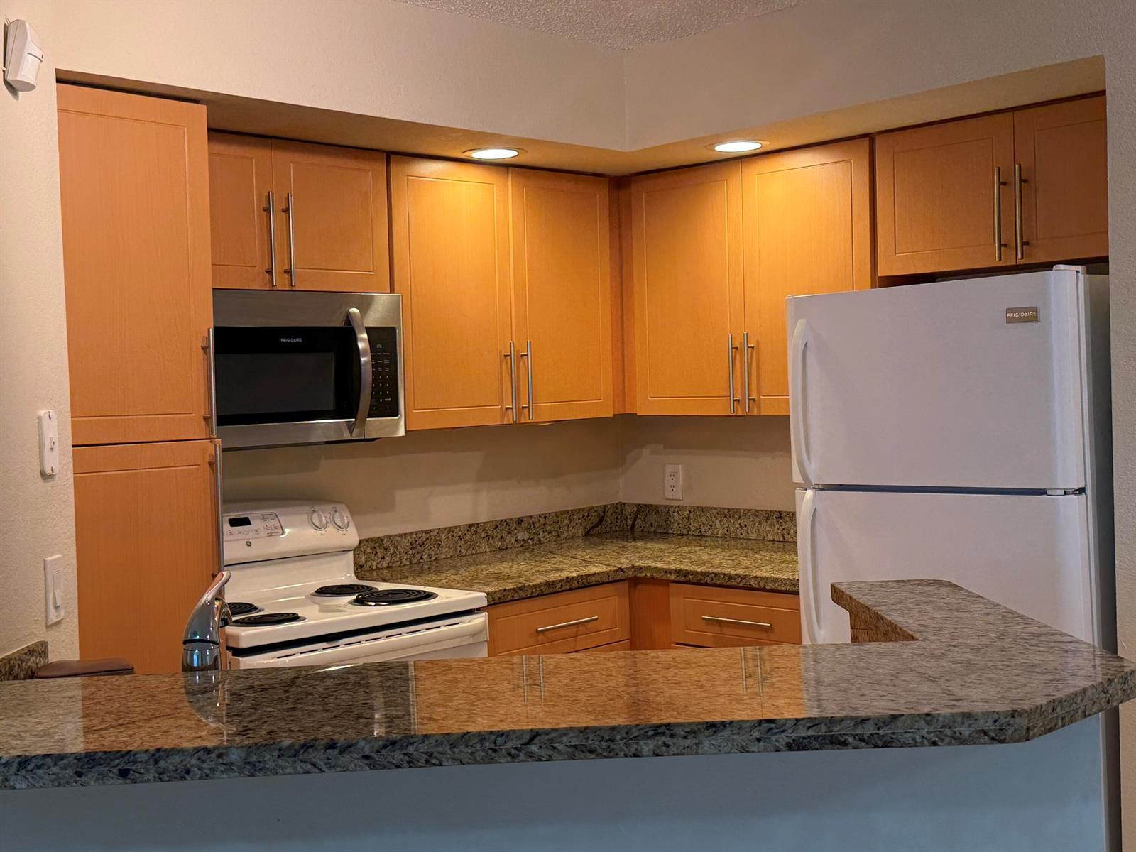A kitchen features light wood cabinets, granite countertops, and stainless steel and white appliances — 3390 N Pinewalk Drive # 1012, Margate FL 33063, MARGATE, FL