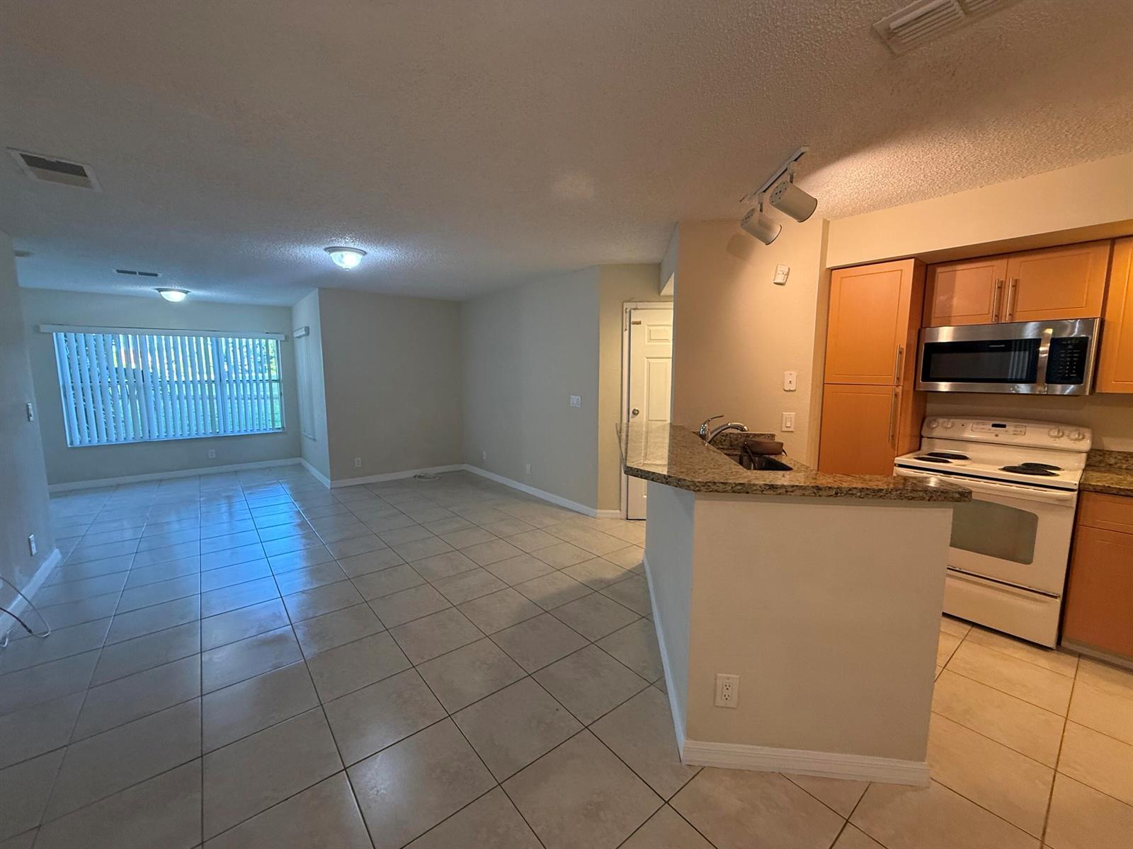 An open-concept living area features tile flooring, a kitchen peninsula, and light-colored cabinetry — 3390 N Pinewalk Drive # 1012, Margate FL 33063, MARGATE, FL