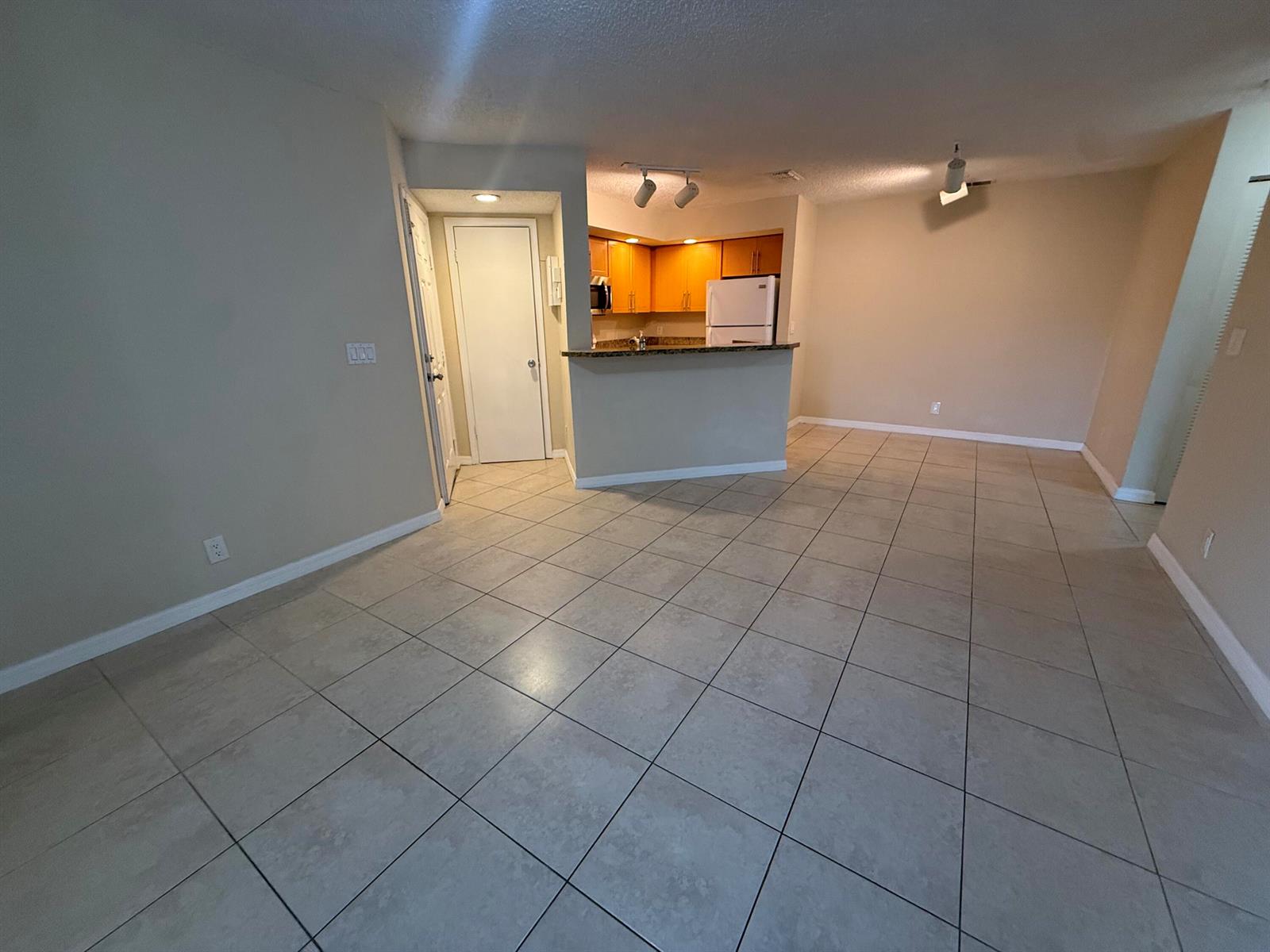 An open-concept living area features beige tile flooring, neutral walls, and a kitchen with wood cabinets — 3390 N Pinewalk Drive # 1012, Margate FL 33063, MARGATE, FL