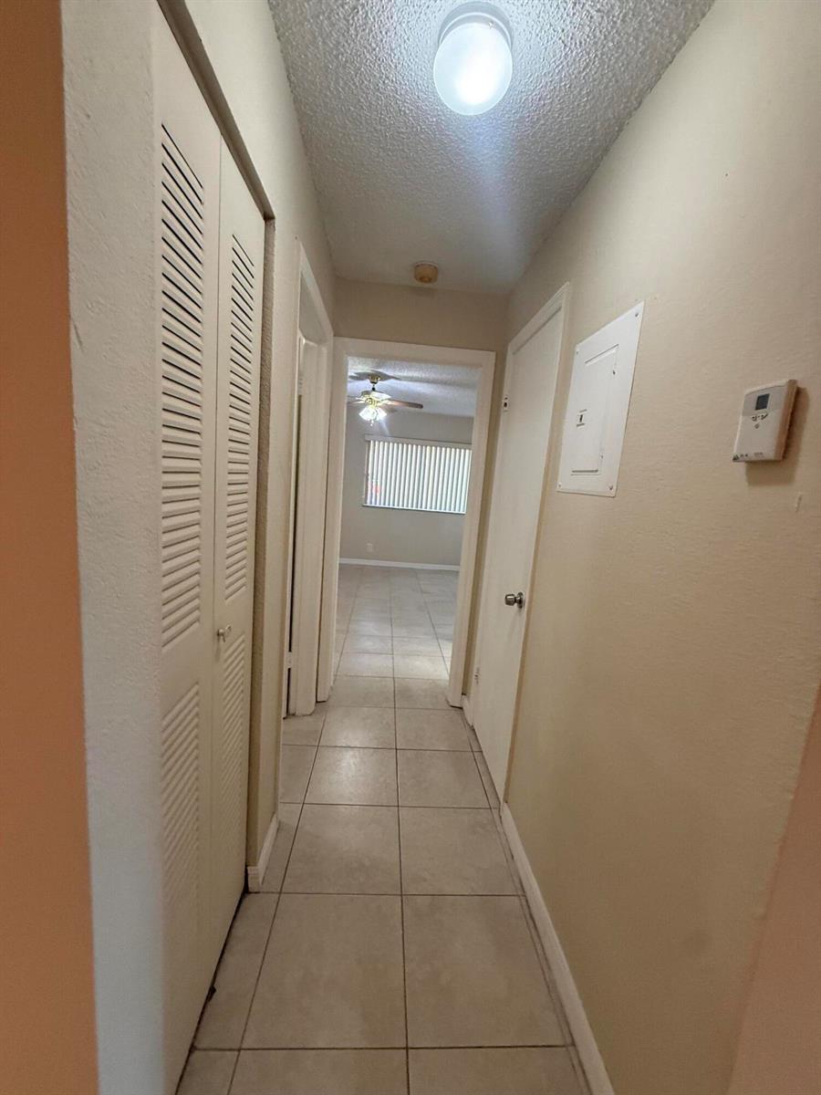 A hallway with tiled flooring leads to a bedroom with a ceiling fan and blinds — 3390 N Pinewalk Drive # 1012, Margate FL 33063, MARGATE, FL