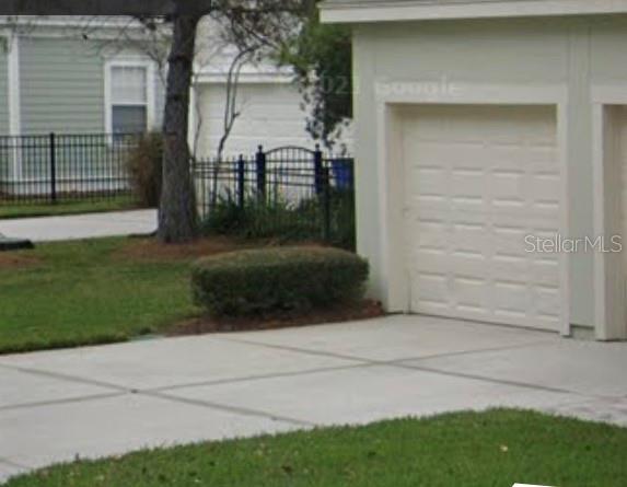 A view of a concrete driveway leading to a white garage door next to landscaping — 848 RUNNER OAK STREET, CELEBRATION, FL