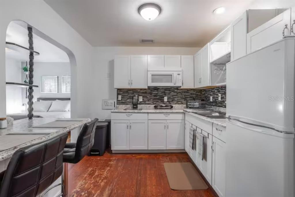 A kitchen with white cabinets, a stone backsplash, and a breakfast bar overlooking a bedroom — 3120 PEEL AVE UNIT 1, ORLANDO, FL