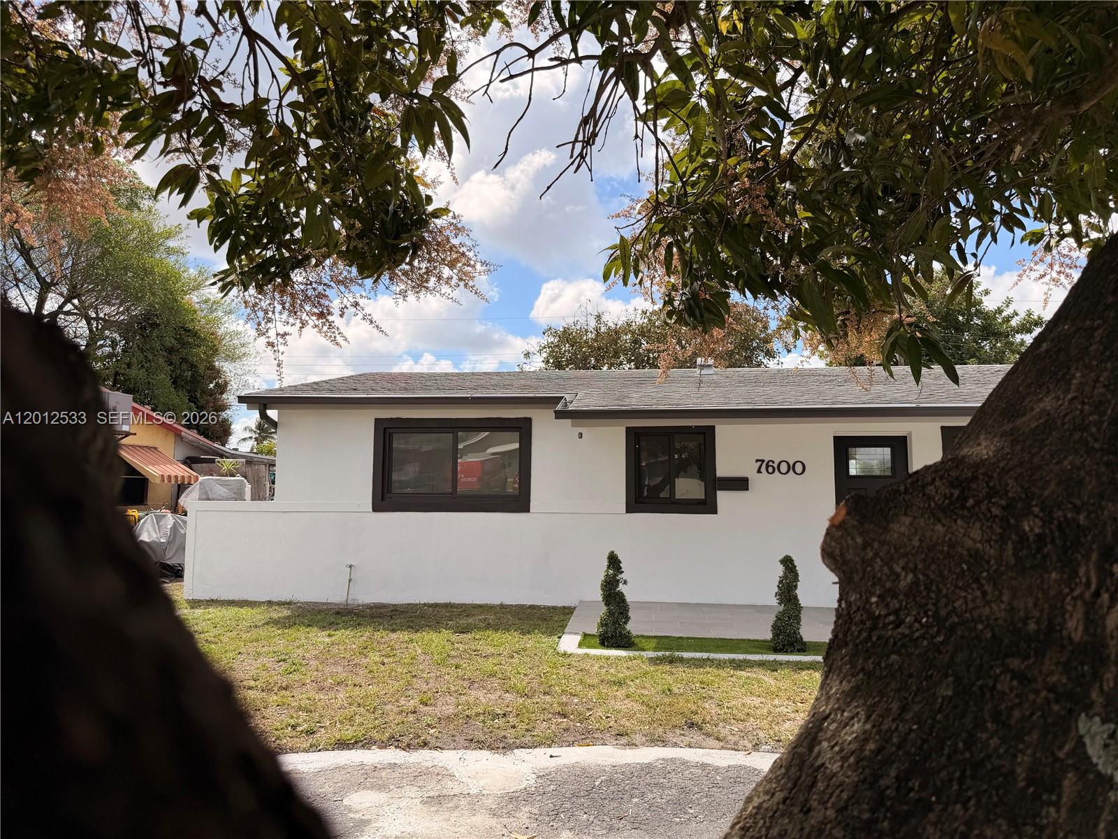 A white single-story house with dark window frames and a front entrance is shown — 7600 Venetian St, Miramar FL 33023, MIRAMAR, FL