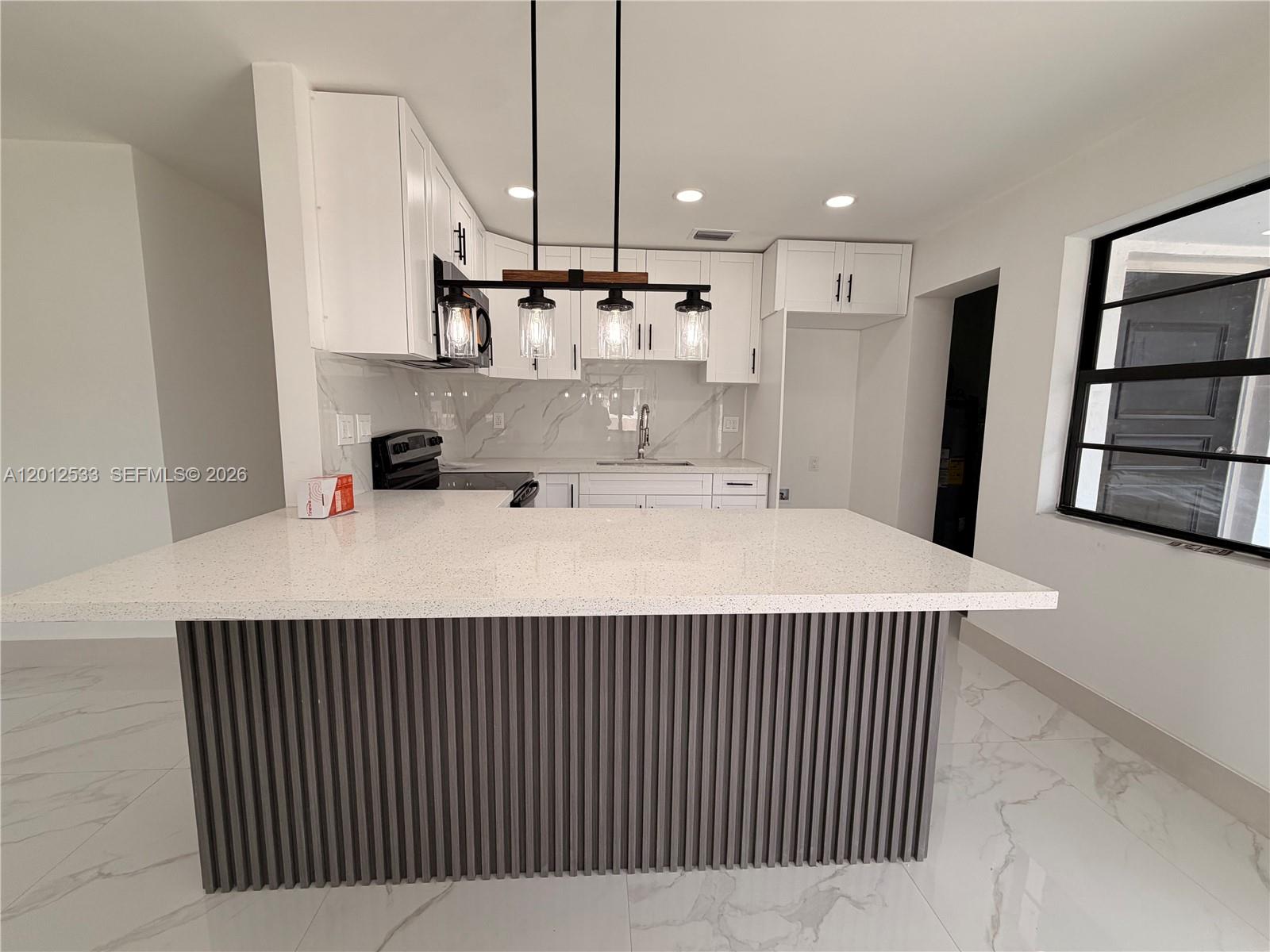 A kitchen features a white quartz peninsula with a gray slatted base and pendant lighting — 7600 Venetian St, Miramar FL 33023, MIRAMAR, FL