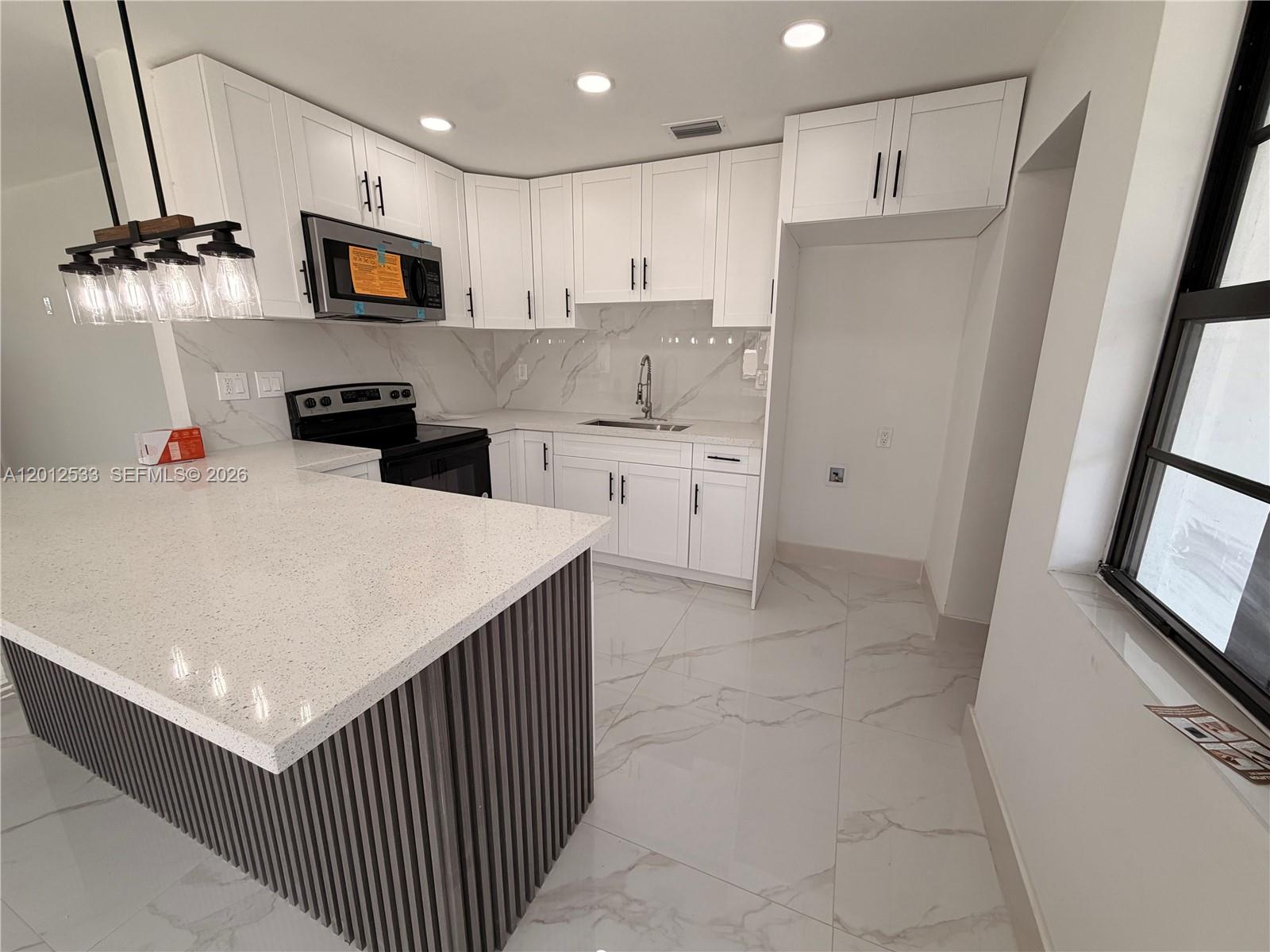 A modern kitchen features white cabinets, quartz countertops, a slatted island, and marble-look tile flooring — 7600 Venetian St, Miramar FL 33023, MIRAMAR, FL