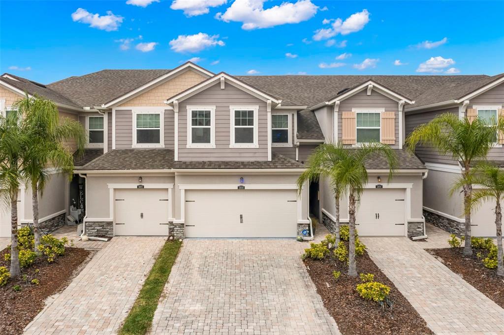 A multi-unit townhouse exterior with beige siding, stone accents, and paved driveways under a blue sky — 5018 SUNNYSIDE LANE, BRADENTON, FL
