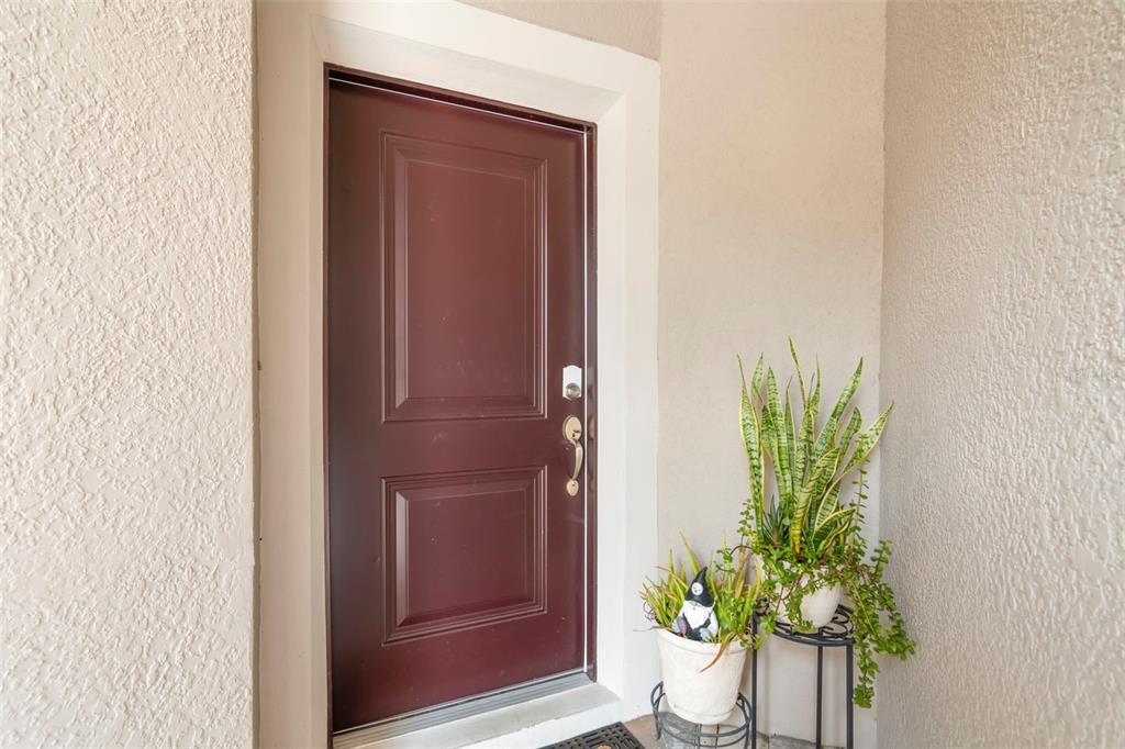 A dark red front door is set in a beige stucco entryway with potted plants — 5018 SUNNYSIDE LANE, BRADENTON, FL