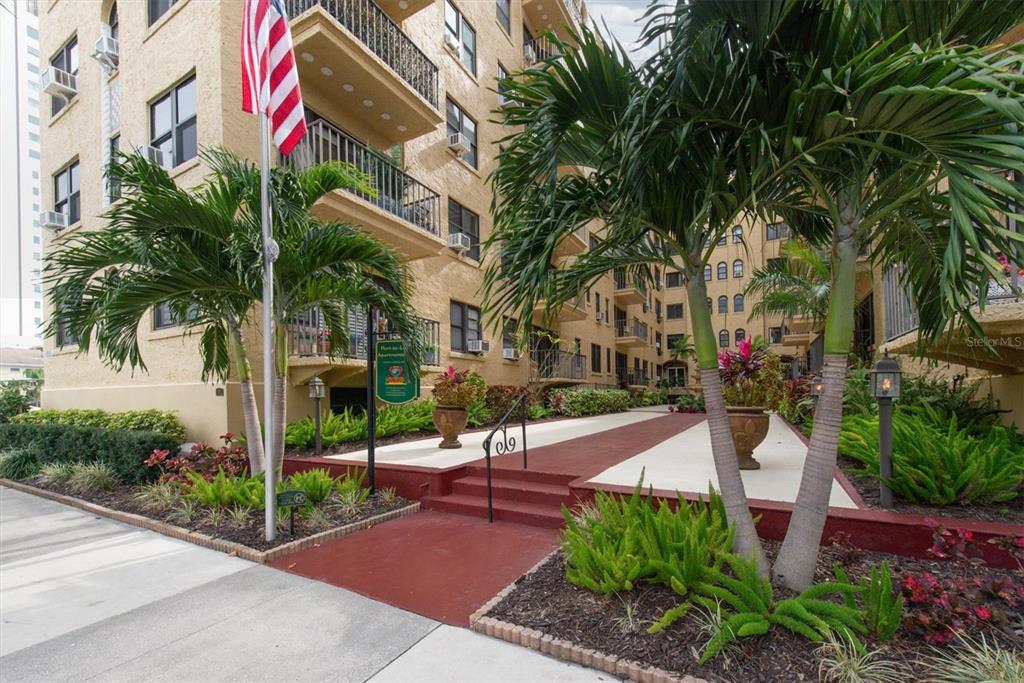 A multi-story apartment building exterior features a red walkway, palm trees, and an American flag — 130 4TH AVENUE N UNIT 201, ST PETERSBURG, FL