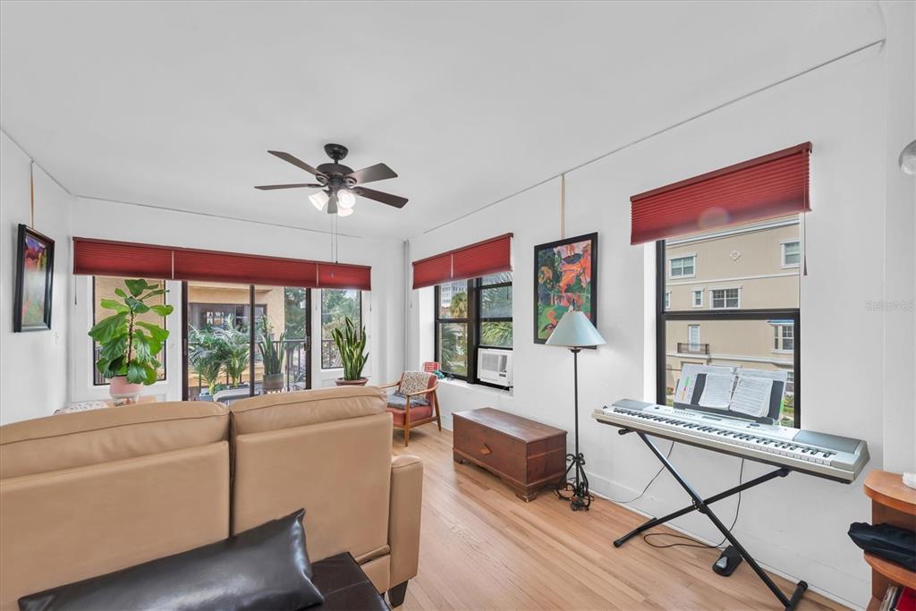 A living room with hardwood floors, a tan sofa, a keyboard, and large windows — 130 4TH AVENUE N UNIT 201, ST PETERSBURG, FL