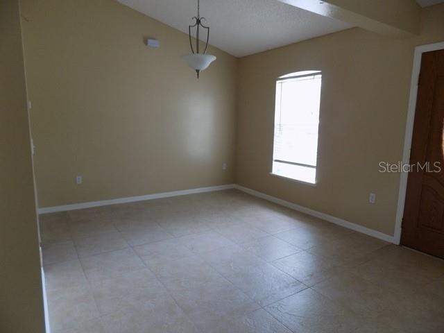 An empty room with beige walls, tile flooring, a hanging light fixture, and a window — 1411 S MARY STREET, EUSTIS, FL