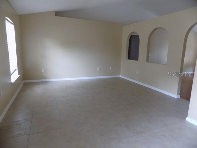 An empty room features beige tile flooring, light-colored walls, and two arched wall cutouts — 1411 S MARY STREET, EUSTIS, FL