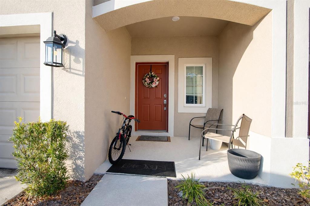 A residential entryway features a red front door, a bicycle, and two patio chairs — 3587 DAVENPORT CREEK COURT, KISSIMMEE, FL