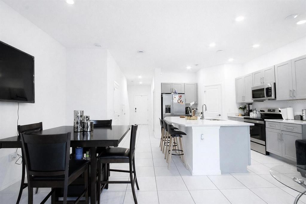 A modern kitchen with gray cabinets, a white island, and an adjacent dining area — 3587 DAVENPORT CREEK COURT, KISSIMMEE, FL