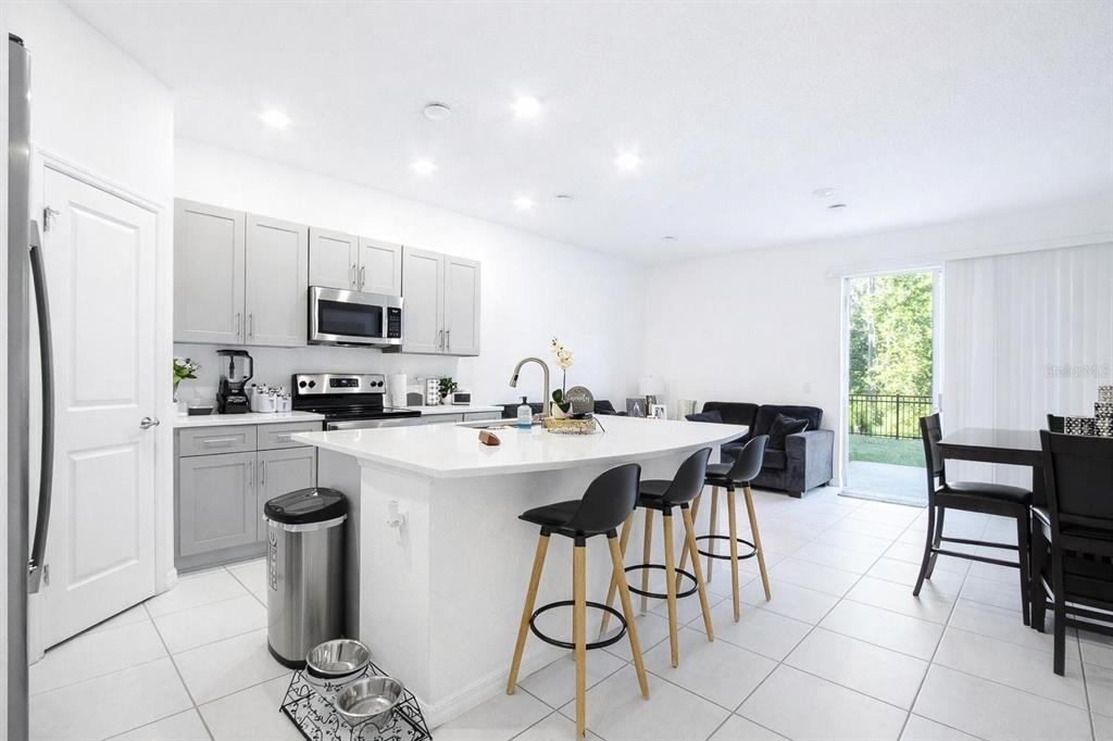 A modern kitchen with light gray cabinets, a white island, and bar stools opens to a living area — 3587 DAVENPORT CREEK COURT, KISSIMMEE, FL