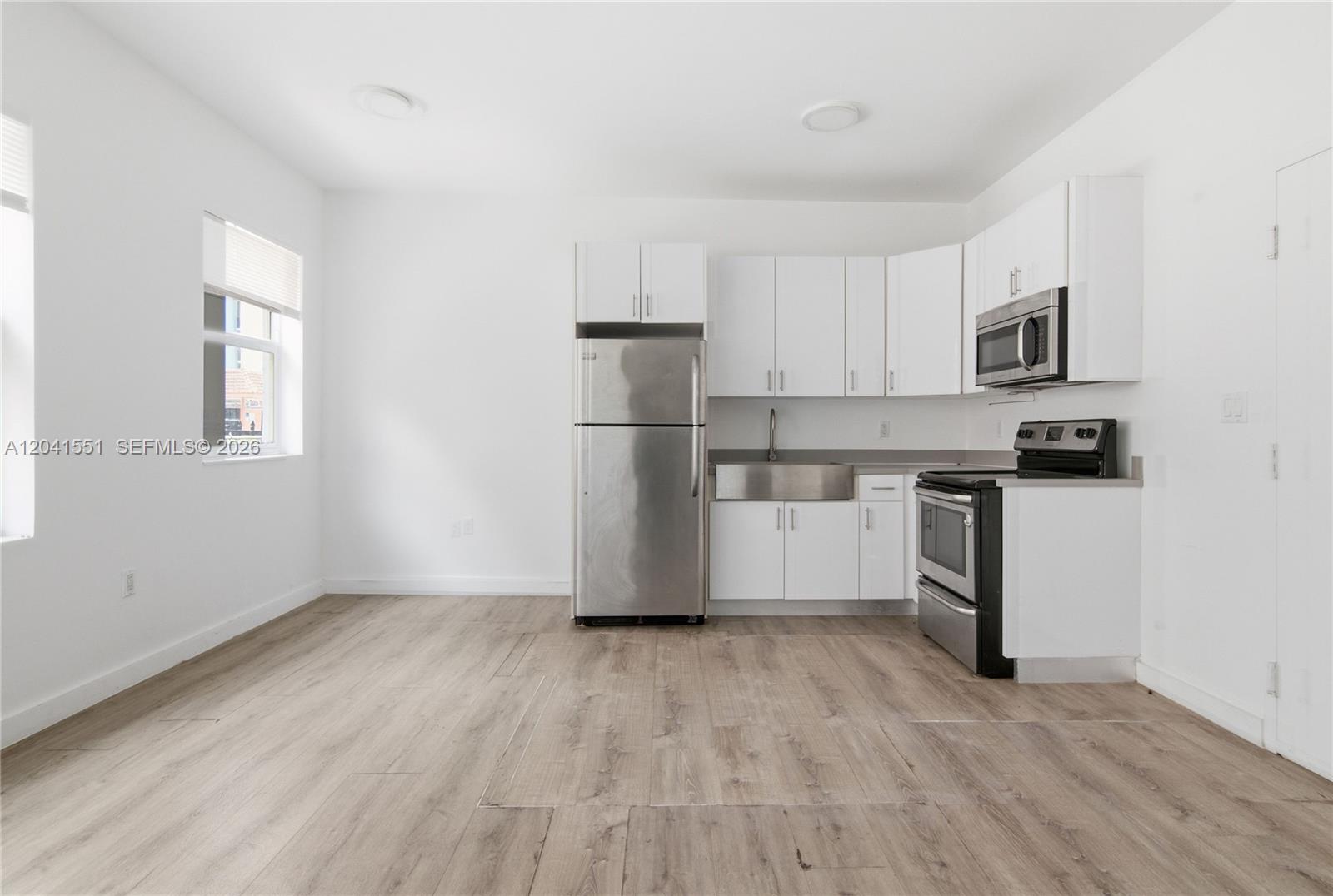 A kitchen features white cabinets, stainless steel appliances, and light wood-look flooring — 402 NW 12th Ave # 111, Miami FL 33128, MIAMI, FL