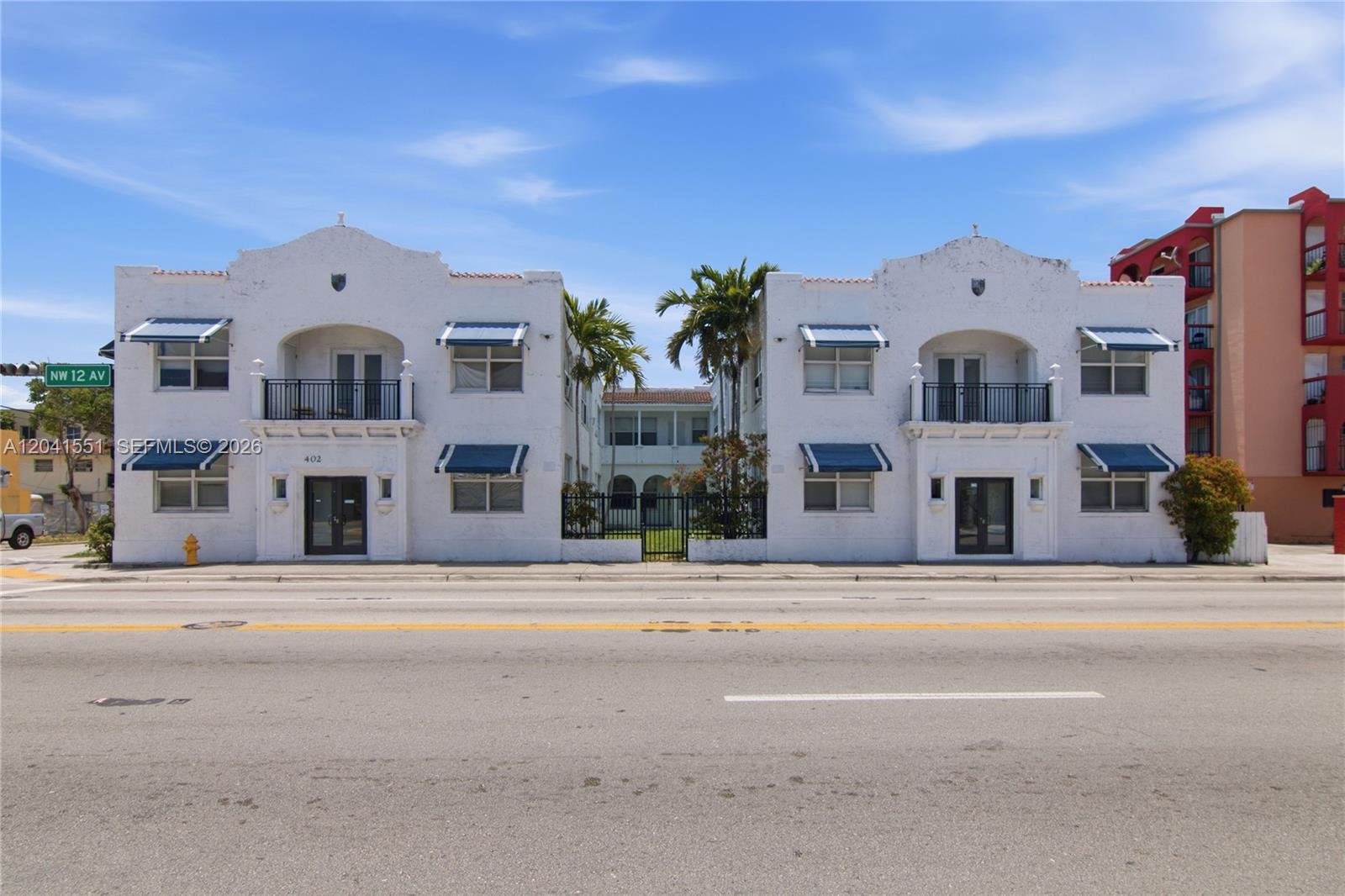 A symmetrical white two-story apartment building features blue awnings and a central gated courtyard — 402 NW 12th Ave # 111, Miami FL 33128, MIAMI, FL