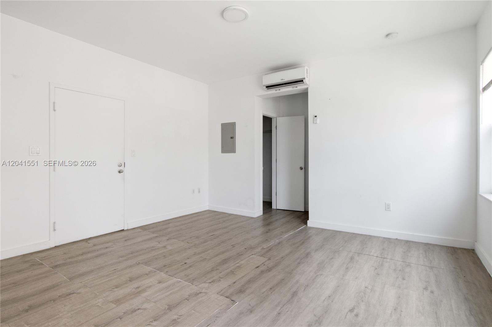 A minimalist room features white walls, light wood-look flooring, and a wall-mounted air conditioner — 402 NW 12th Ave # 111, Miami FL 33128, MIAMI, FL