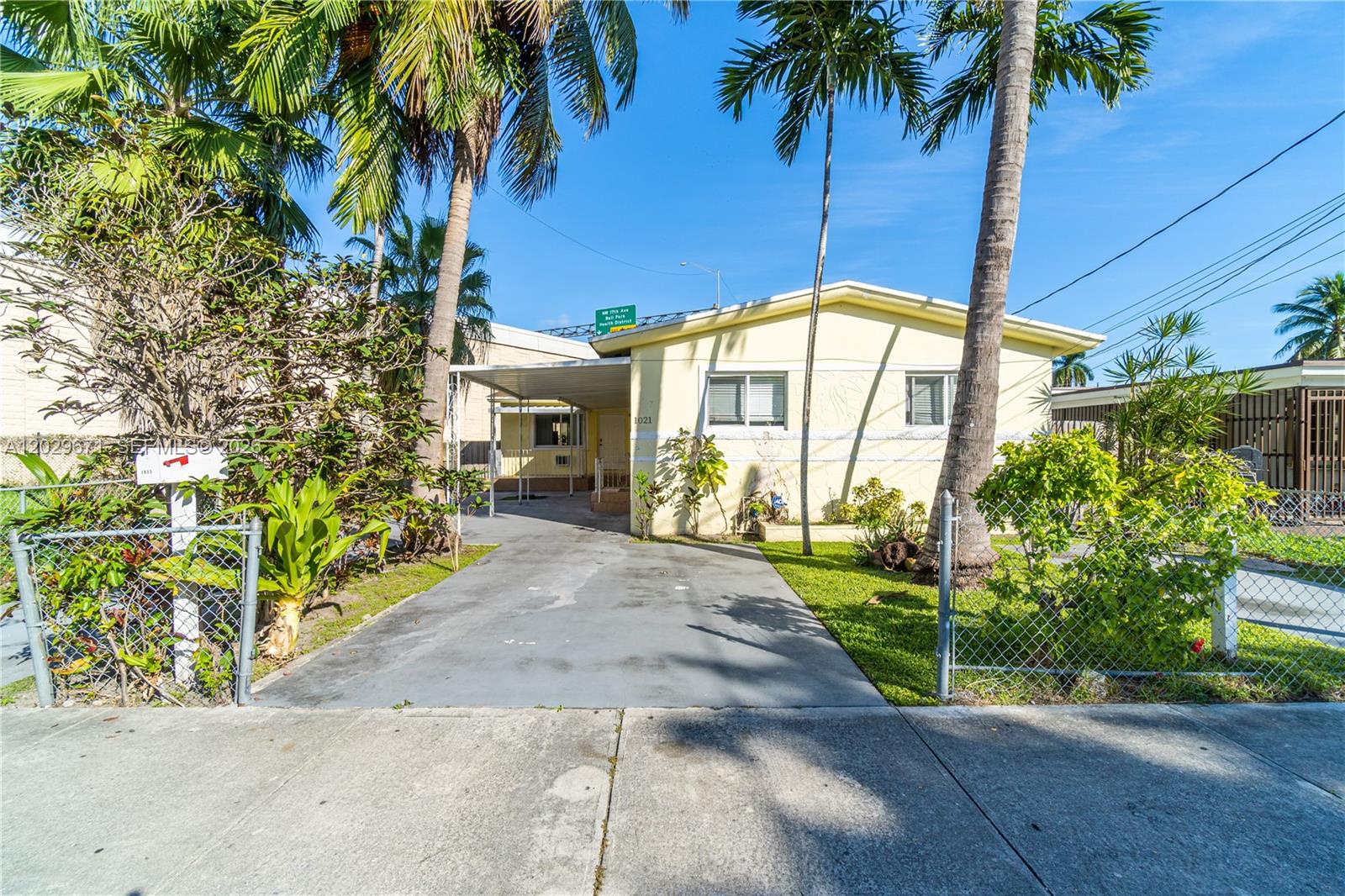 A yellow single-story house features a concrete driveway, a carport, and a chain-link fence — 1021 NW 23rd Ave # 1023, Miami FL 33125, MIAMI, FL
