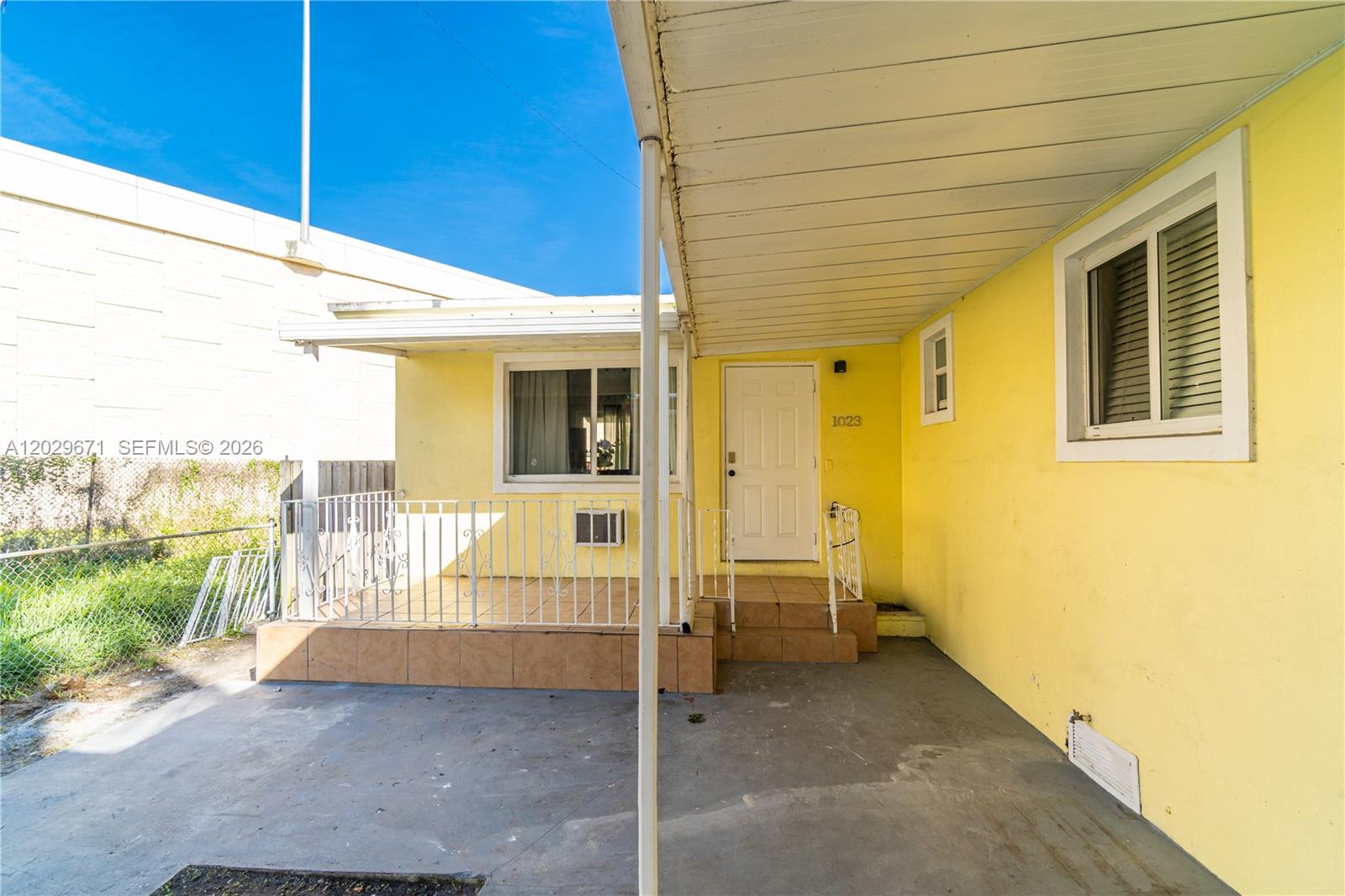 A yellow house exterior features a covered porch, a white door, and a tiled patio — 1021 NW 23rd Ave # 1023, Miami FL 33125, MIAMI, FL