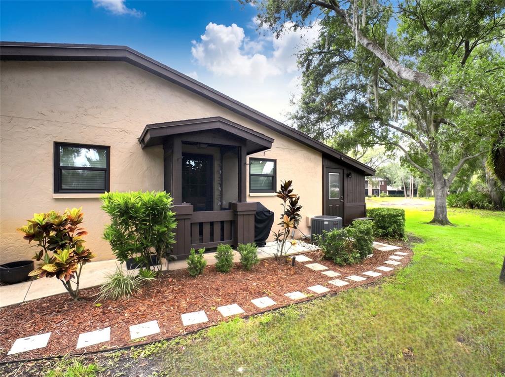 The exterior of a tan house features a dark brown porch, landscaping, and stone pavers — 1400 TARPON WOODS BOULEVARD UNIT A1, PALM HARBOR, FL