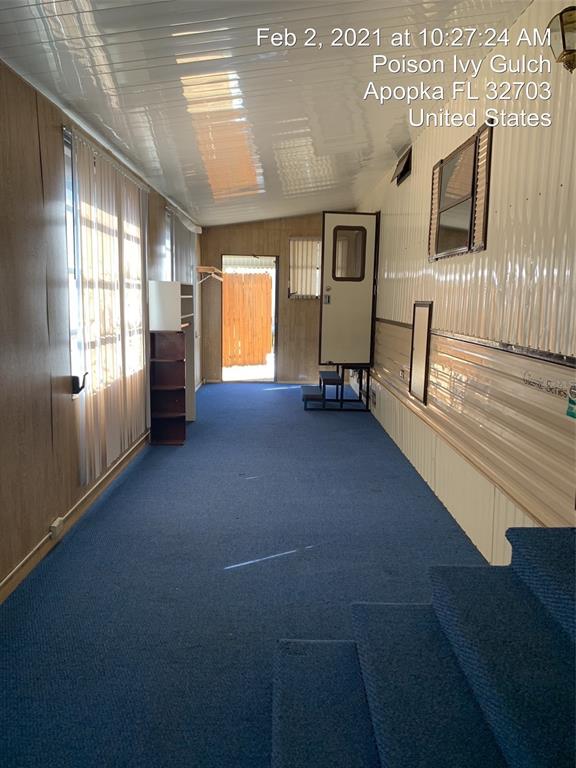 A long, narrow room with blue carpeting, wood-paneled walls, and a door leading outside — 3000 CLARCONA ROAD UNIT 616, APOPKA, FL
