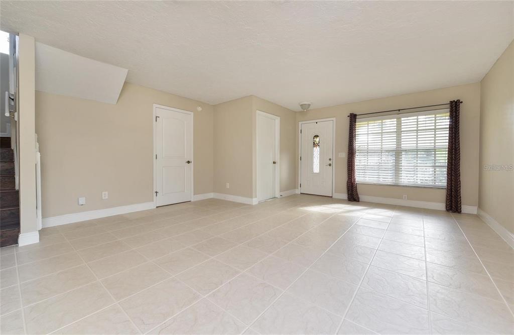 An empty living room features beige tile flooring, light-colored walls, and a white front door — 9551 CHANDON DRIVE, ORLANDO, FL
