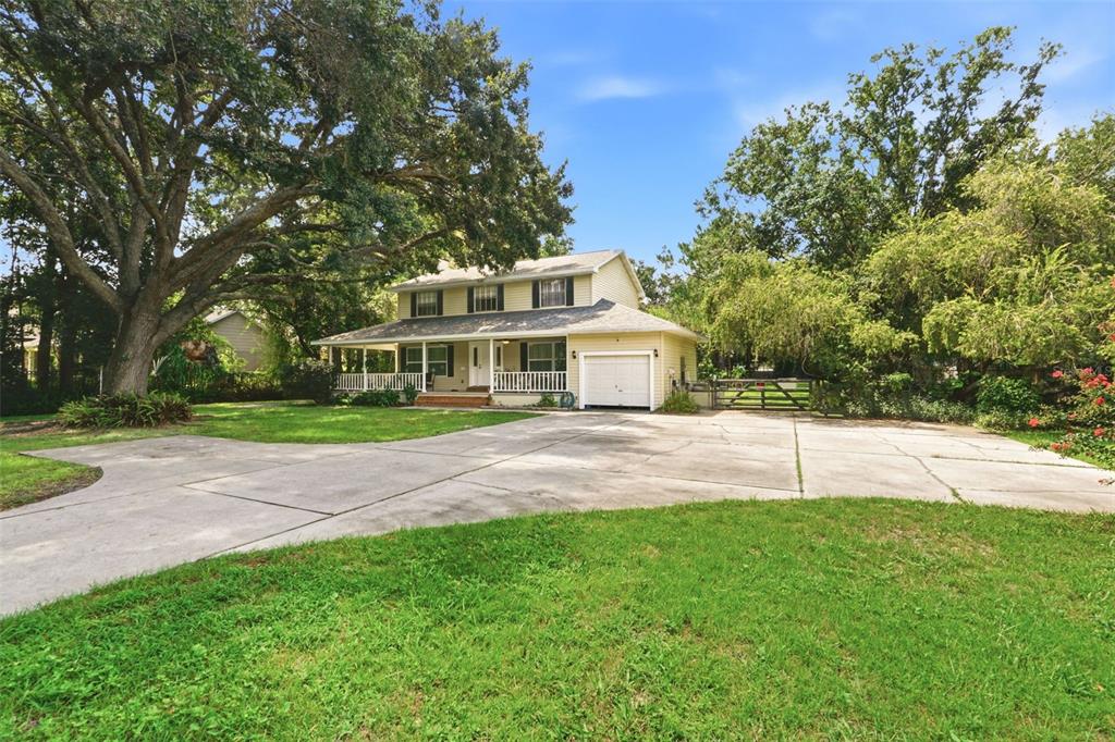 A two-story yellow house with a front porch and attached garage sits behind a concrete driveway — 4784 OREN BROWN ROAD, KISSIMMEE, FL