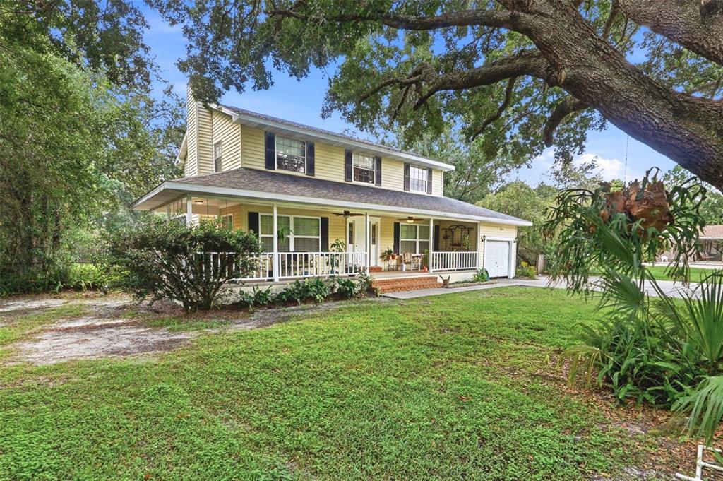 A two-story yellow house with a wrap-around porch sits on a grassy, tree-shaded lot — 4784 OREN BROWN ROAD, KISSIMMEE, FL