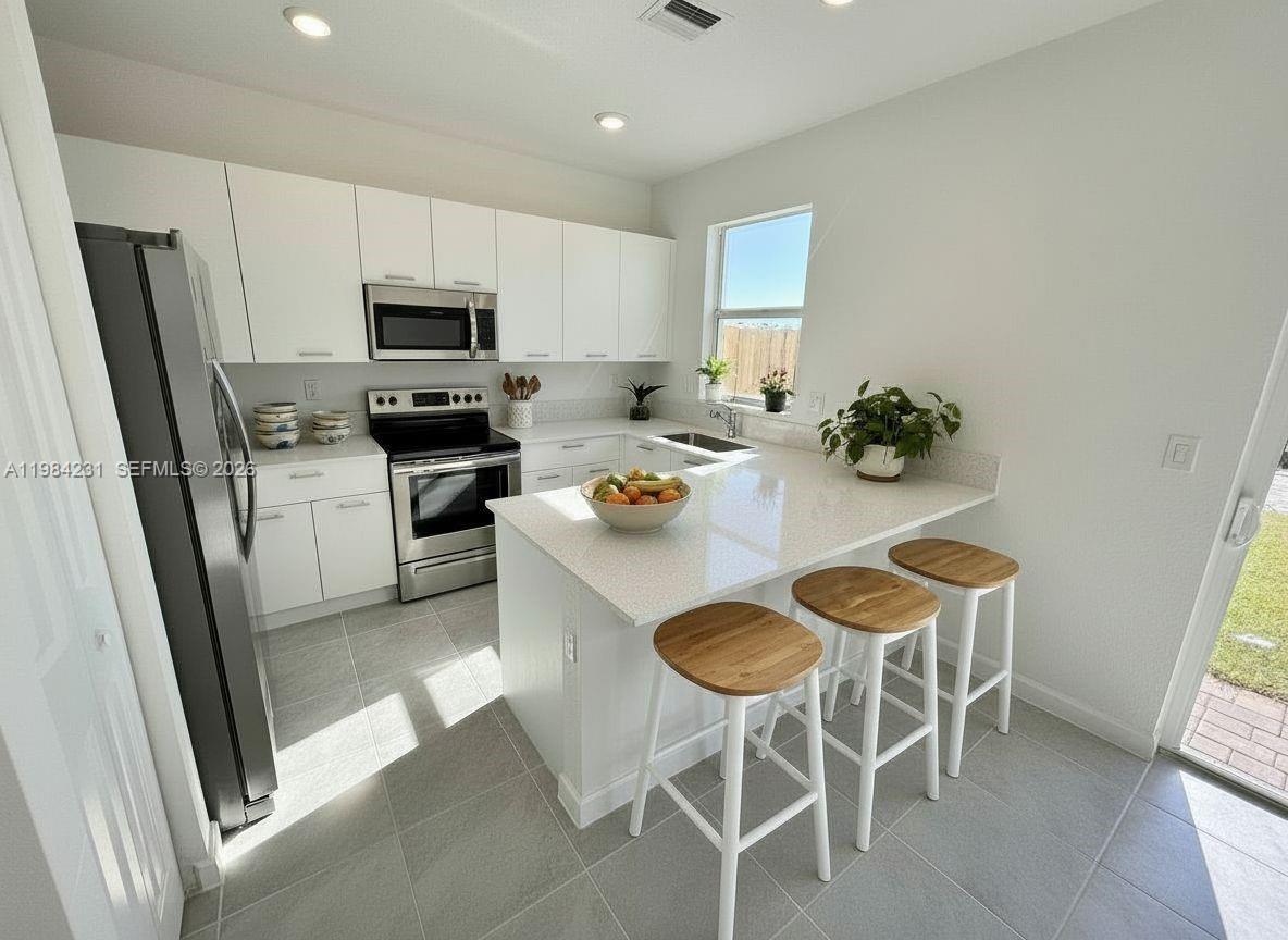 A modern kitchen features white cabinetry, stainless steel appliances, and a quartz-topped breakfast bar — 12354 NW 23rd Ct, Miami FL 33167, MIAMI, FL