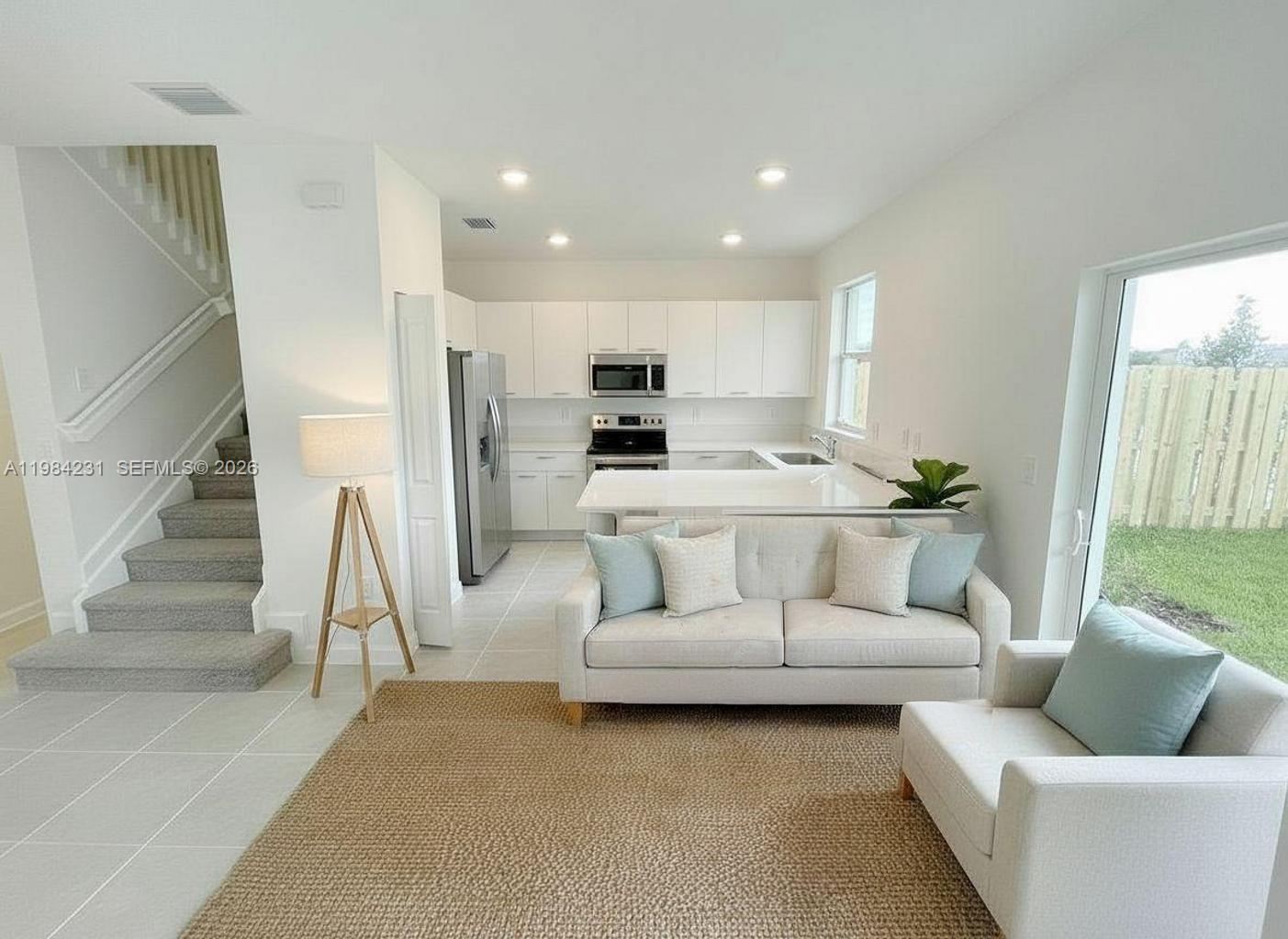 A modern open-concept living room and kitchen featuring white cabinetry, stainless appliances, and carpeted stairs — 12354 NW 23rd Ct, Miami FL 33167, MIAMI, FL